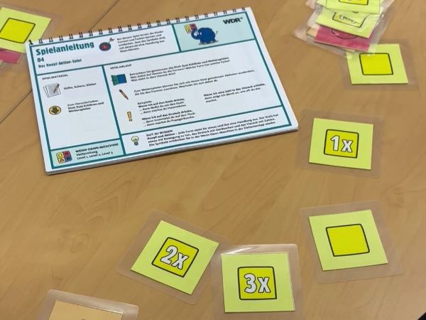 Eine Mappe mit Spielanleitungen sowie Spielkarten liegen auf dem Tisch.