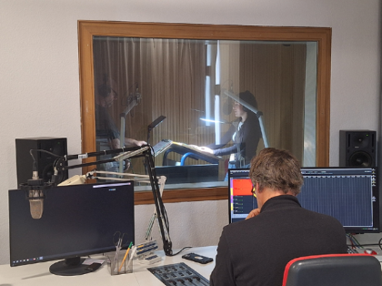 Zwei Menschen in einer Sprecherkabine bei einer Sprachaufnahme im Tonstudio.