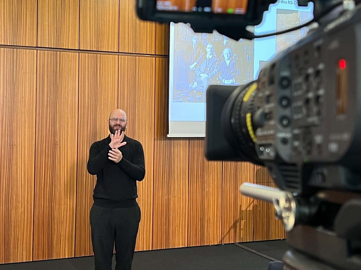 Ein Kamerateam des LVR‑ZMB zeichnet die Gedenkveranstaltung im Rheinlandsaal auf, während DGS‑Dolmetscher*innen die Beiträge live begleiten.