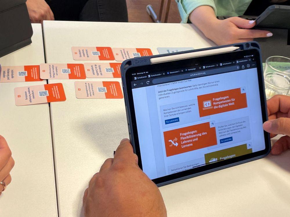 Eine Schulentwicklungsgruppe mit einer im Beratungsgespräch etablierten Kartenaufstellung: die ausgewählten Karten liegen auf dem Tisch und die darauf sichtbaren QR Codes führen zu passenden Fragebögen auf der Onlineplattform.