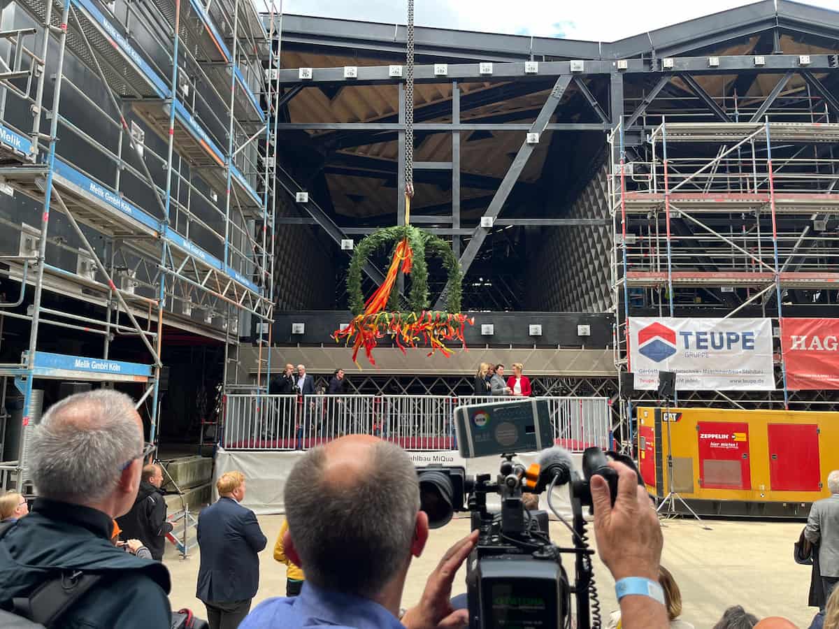 Kamerateam filmt das Richtfest, im Hintergrund ein Gebäude im Bau.	