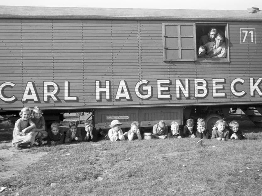 Kinder liegen unter einem Zirkuswagen.