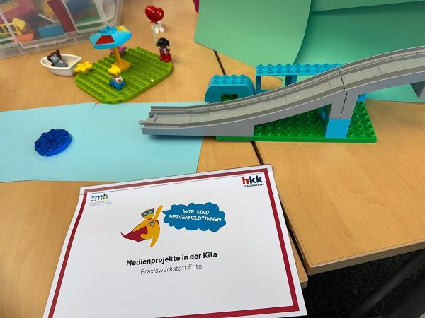 Auf einem Tisch liegen Legobauteile und eine Broschüre mit dem Titel "Medienprojekte in der Kita. Praxiswerkstatt Foto."