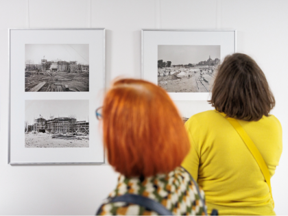 Zwei Frauen sehen sich gerahmte Fotos an, die an einer Wand hängen. Zwei Frauen sehen sich gerahmte Fotos an, die an einer Wand hängen.