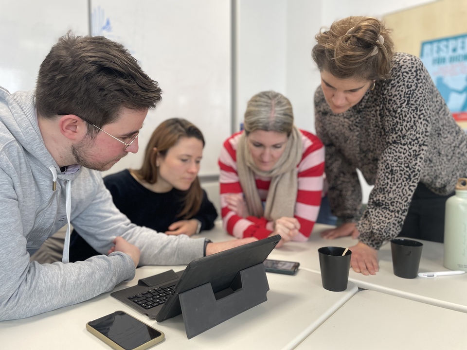 Vier Lehrkräfte blicken während einer Arbeitsphase gemeinsam auf ein Smartphone.