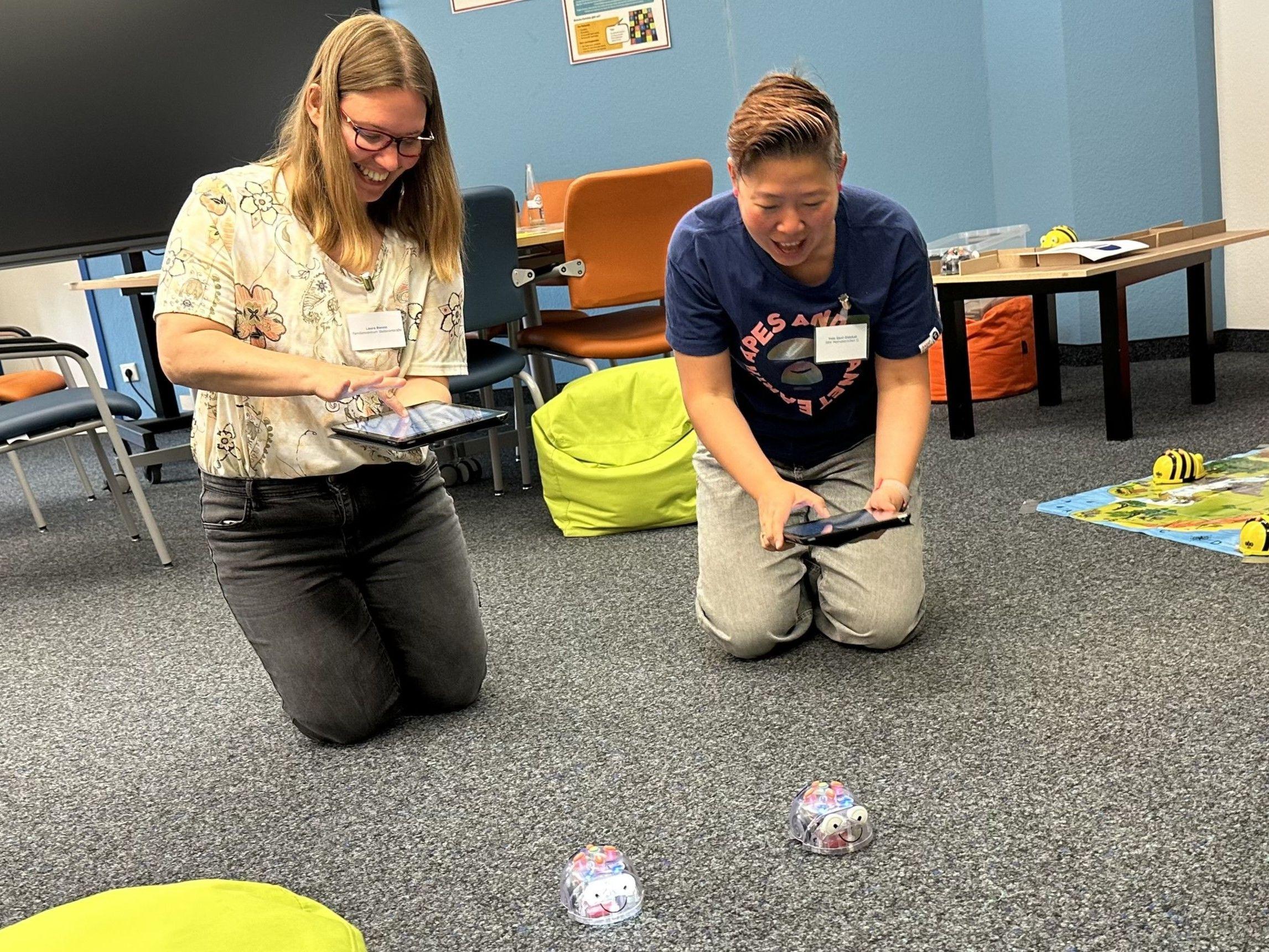 Zwei Teilnehmerinnen lachen beim Spiel mit den Blue-Bots und veranstalten ein Wettrennen. Zwei Teilnehmerinnen lachen beim Spiel mit den Blue-Bots und veranstalten ein Wettrennen.
