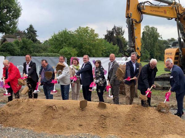11 Personen mit Spaten an einer Baustelle.	 11 Personen mit Spaten an einer Baustelle.