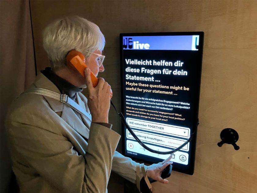 Eine Frau hält einen Telefonhörer der mit einem Touchbildschirm verbunden ist. Eine Frau hält einen Telefonhörer der mit einem Touchbildschirm verbunden ist.